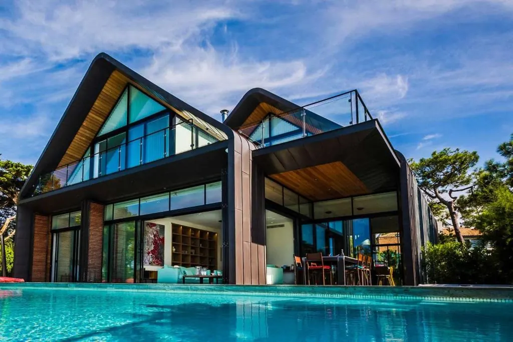 Piscine au pied d'une villa contemporaine en bardage sombre, le ciel bleu se reflète dans l'eau